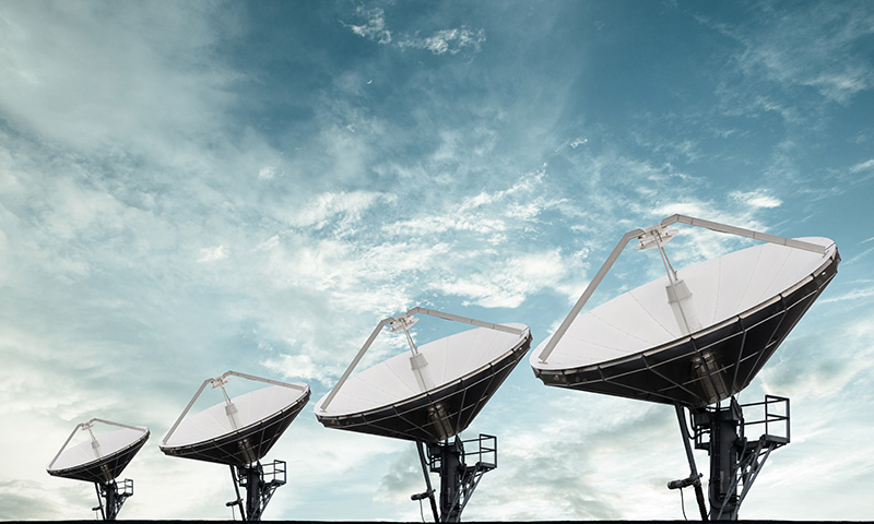 A képen nagy méretű, parabola alakú, földfelszíni rádiótávközlési antennák láthatók egymás után, sorban, felhős ég alatt.
