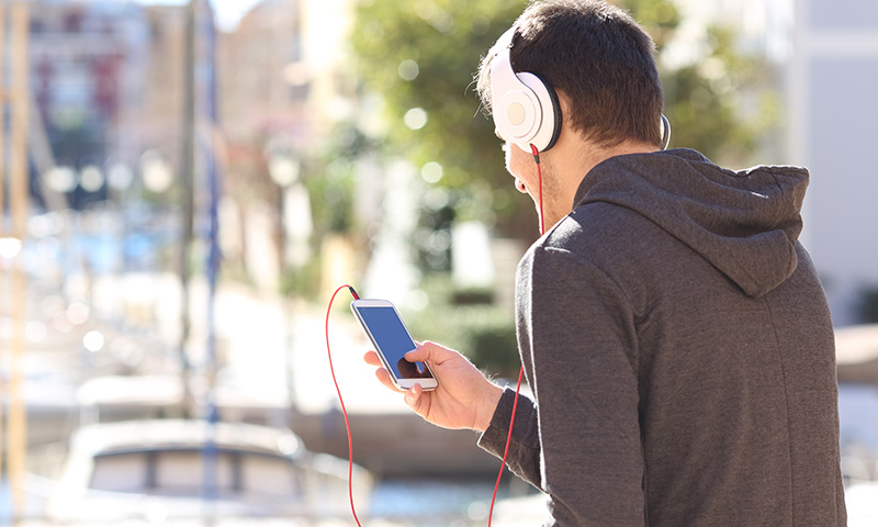 Fiatal férfi mobilon zenét hallgat egy kikötőben